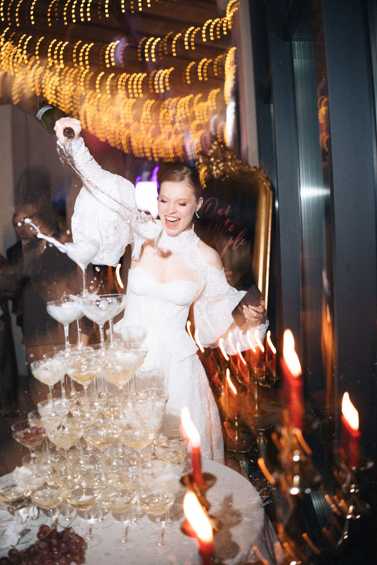 A champagne tower being poured at an elegant event with glowing lights and white feather decorations.