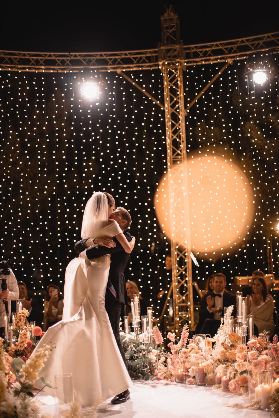 A romantic first dance moment captured against a backdrop of sparkling lights and floral decorations.