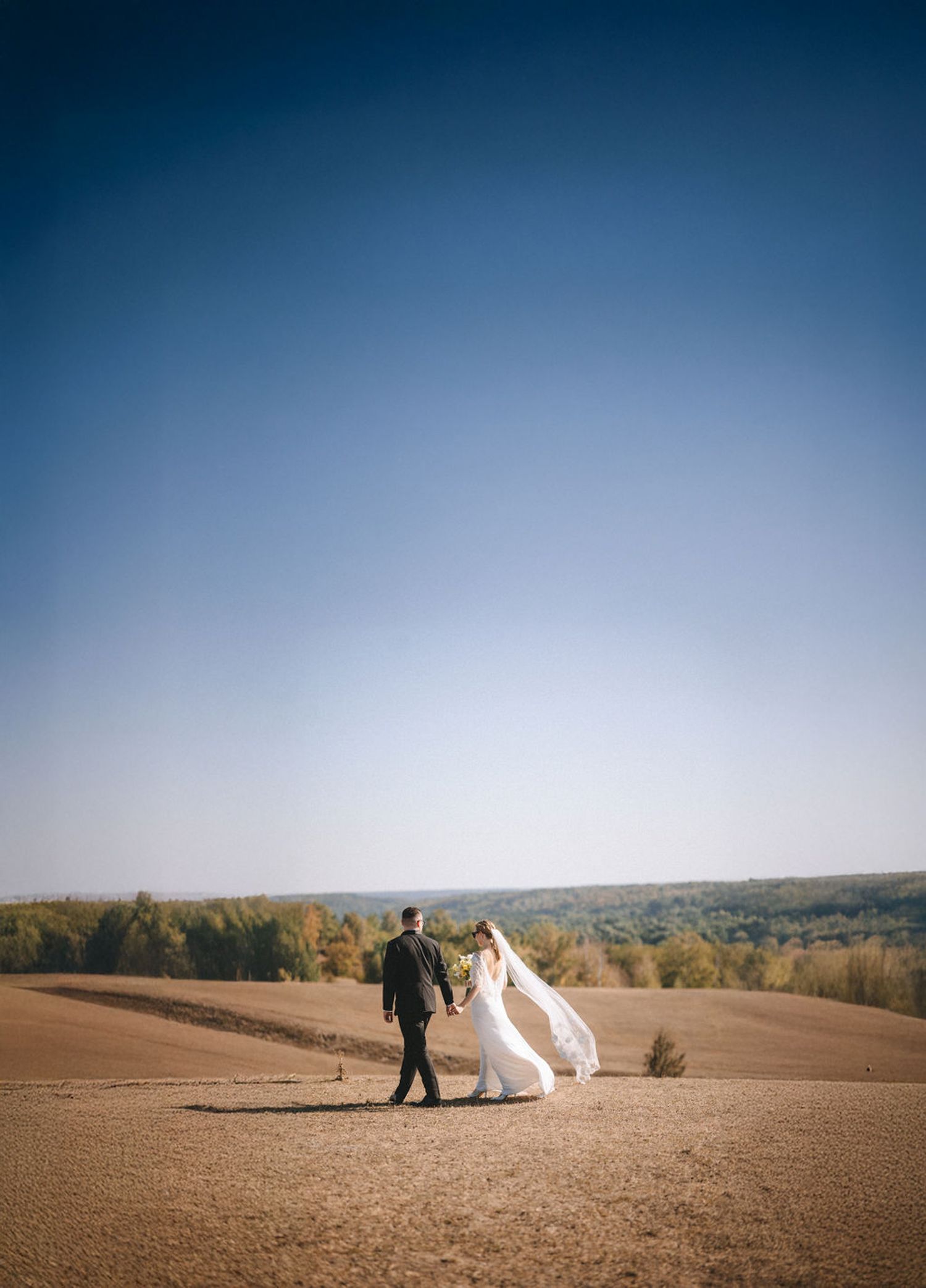 A couple poses together on sandy desert dunes during sunset with dramatic sky in the background.