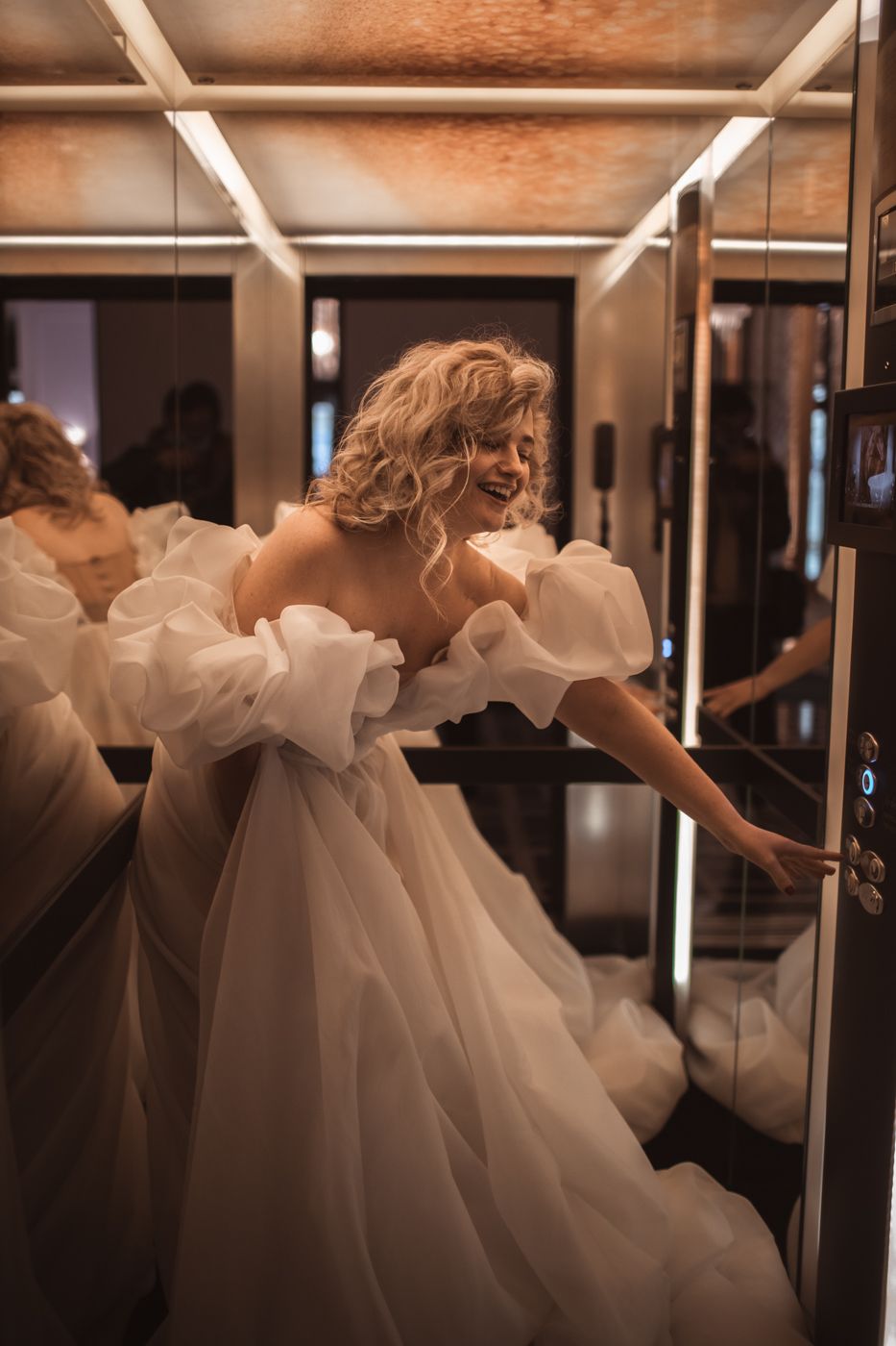 Woman in puffy white wedding dress twirls playfully in mirrored room.