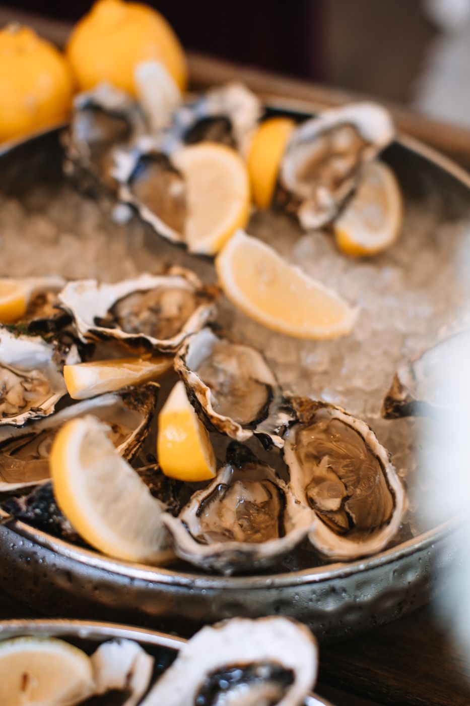 Fresh oysters on ice garnished with lemon wedges served on a white plate.