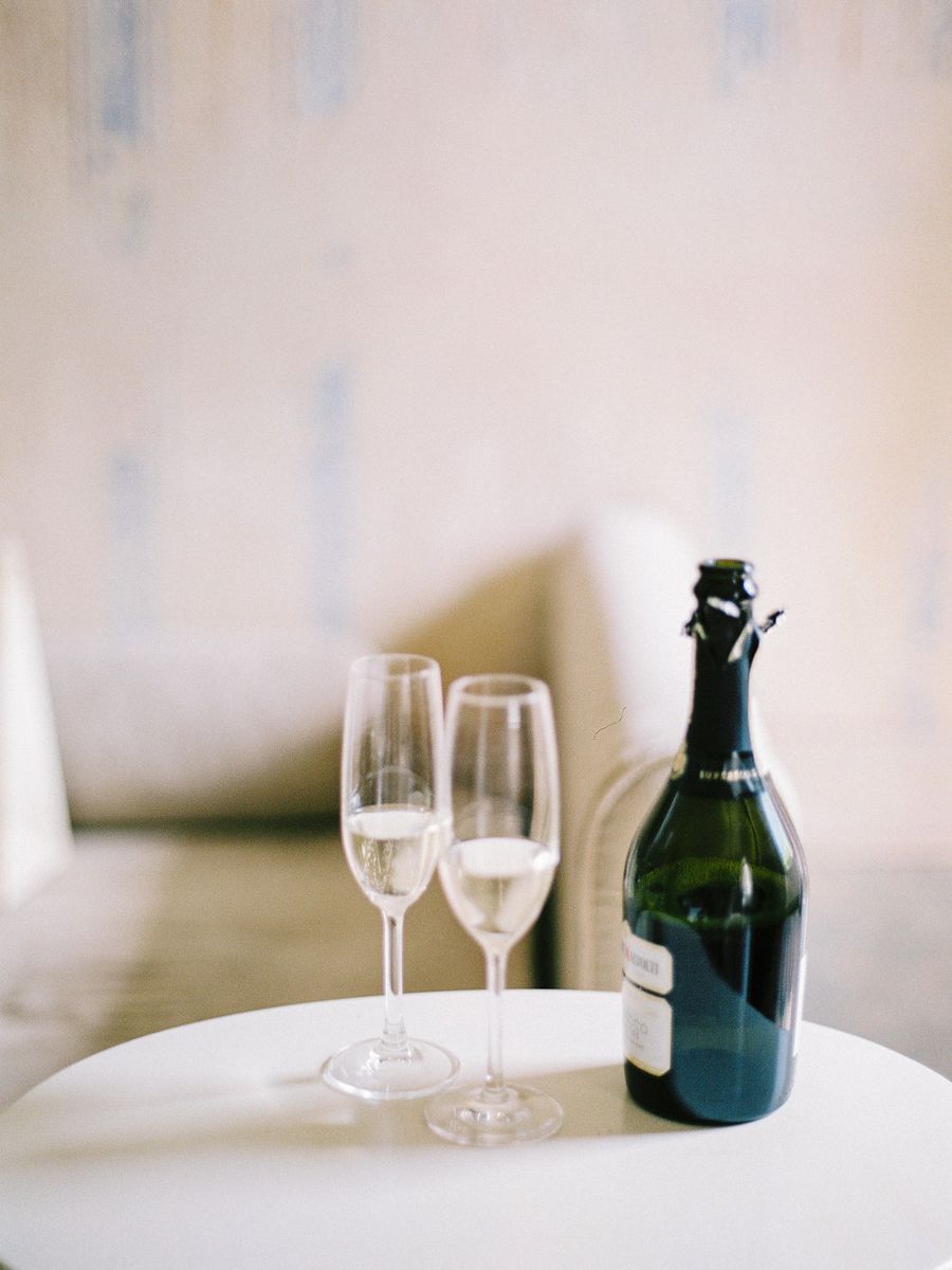 A series of wine glasses and dark bottles arranged in a minimalist style on a white surface against a light background.