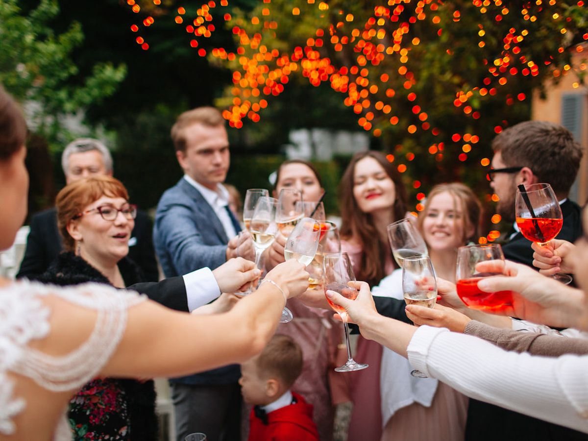 Wedding guests raise champagne glasses in a celebratory toast under twinkling outdoor lights.