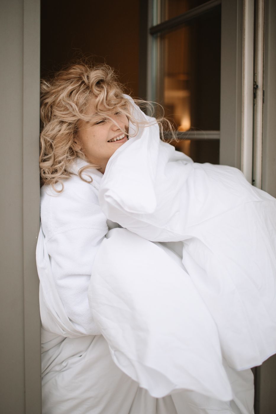 Candid moment of joy captured as person in white robe laughs near window.