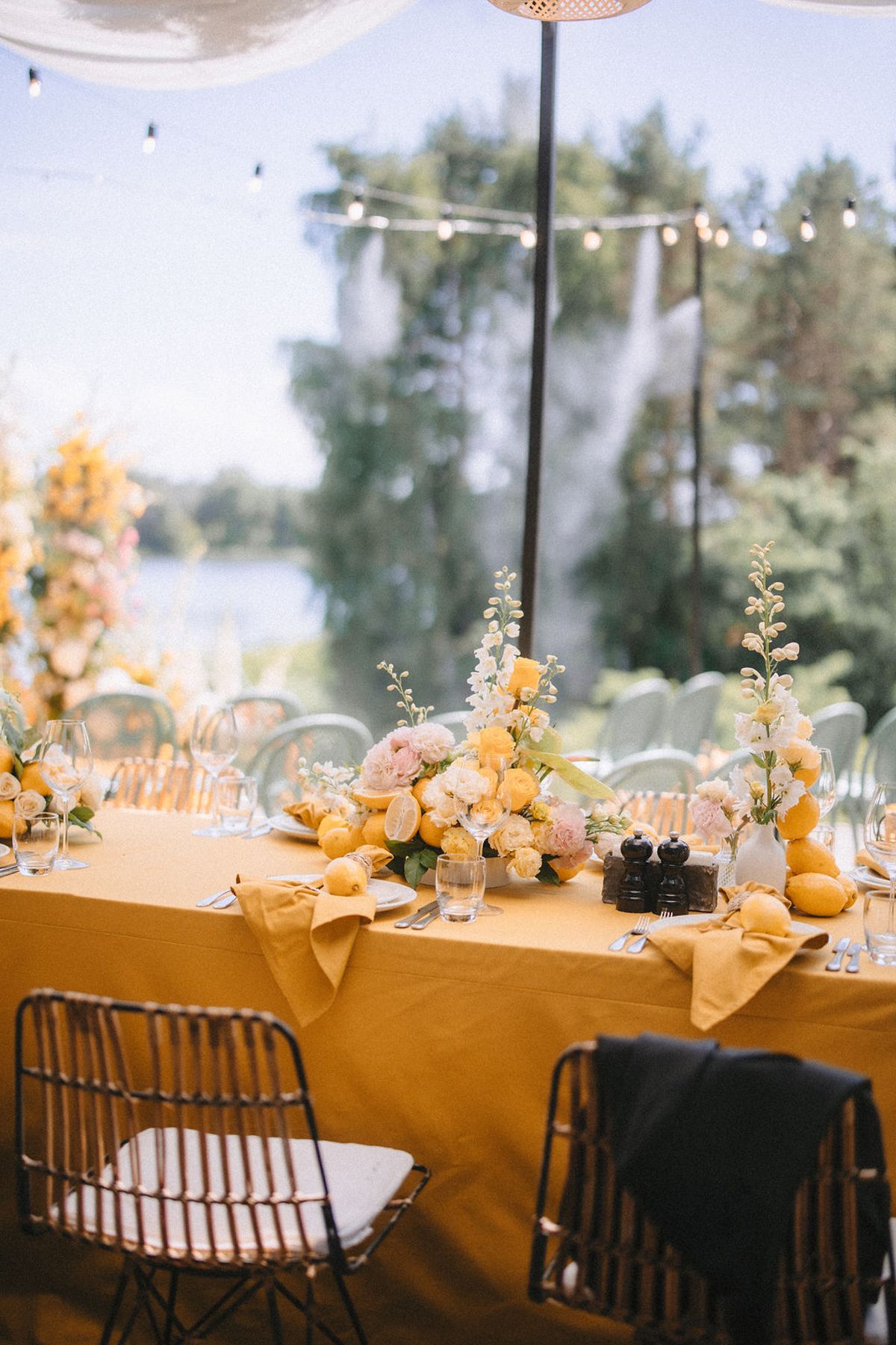 Elegant wedding reception tables with yellow tablecloths and floral centerpieces set against a bright outdoor backdrop.