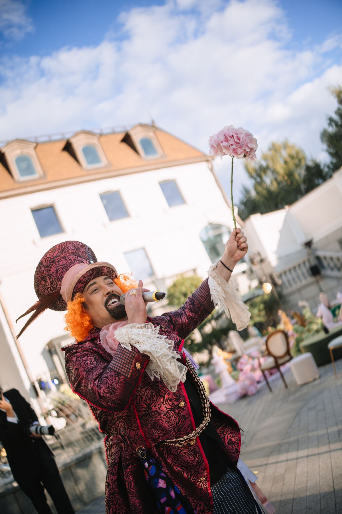 A person in a decorative burgundy costume with a mask performs at an outdoor festival against a blue sky background.