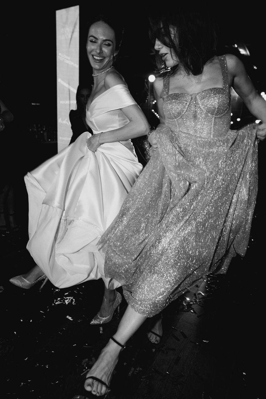 People dancing in formal attire with sparkly dresses on a dark dance floor.