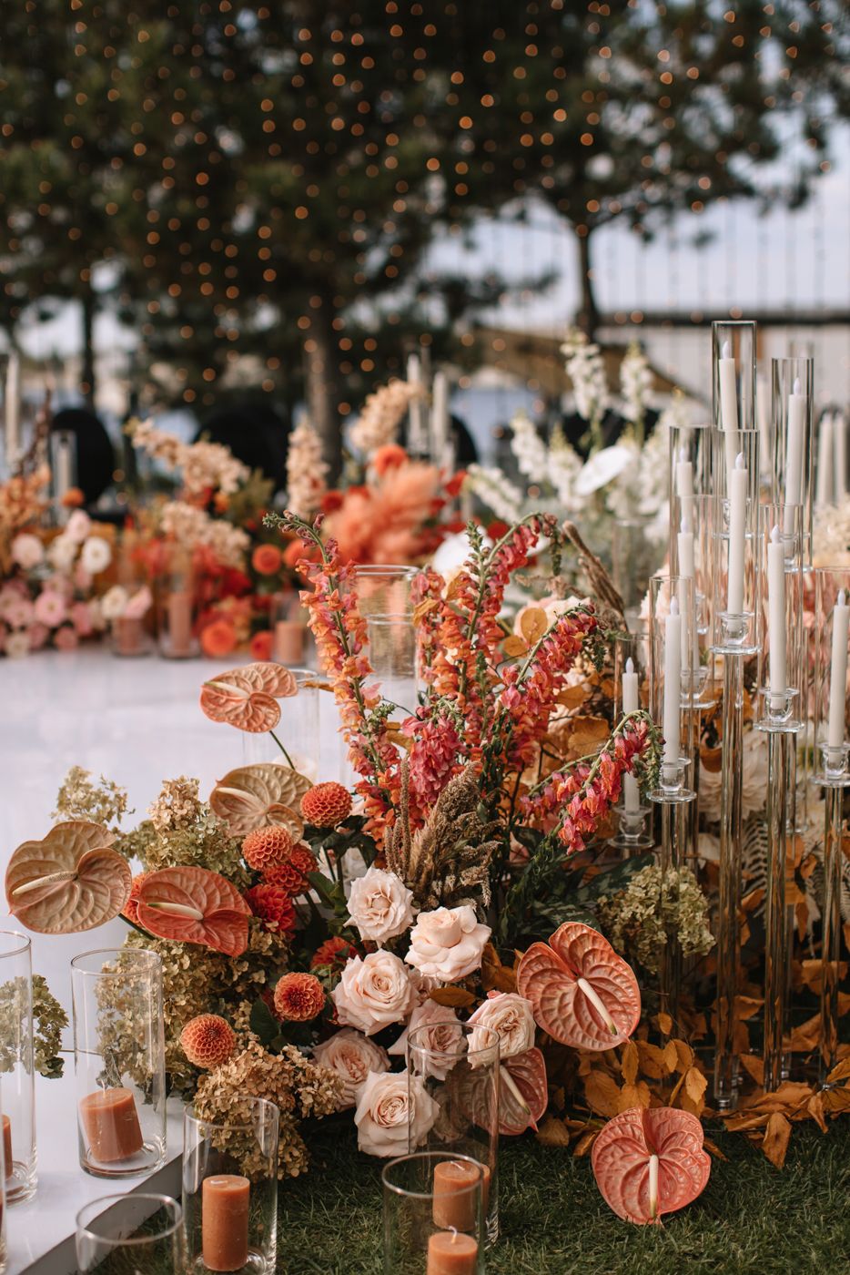 Outdoor wedding decor featuring coral and peach floral arrangements with glass candle holders.