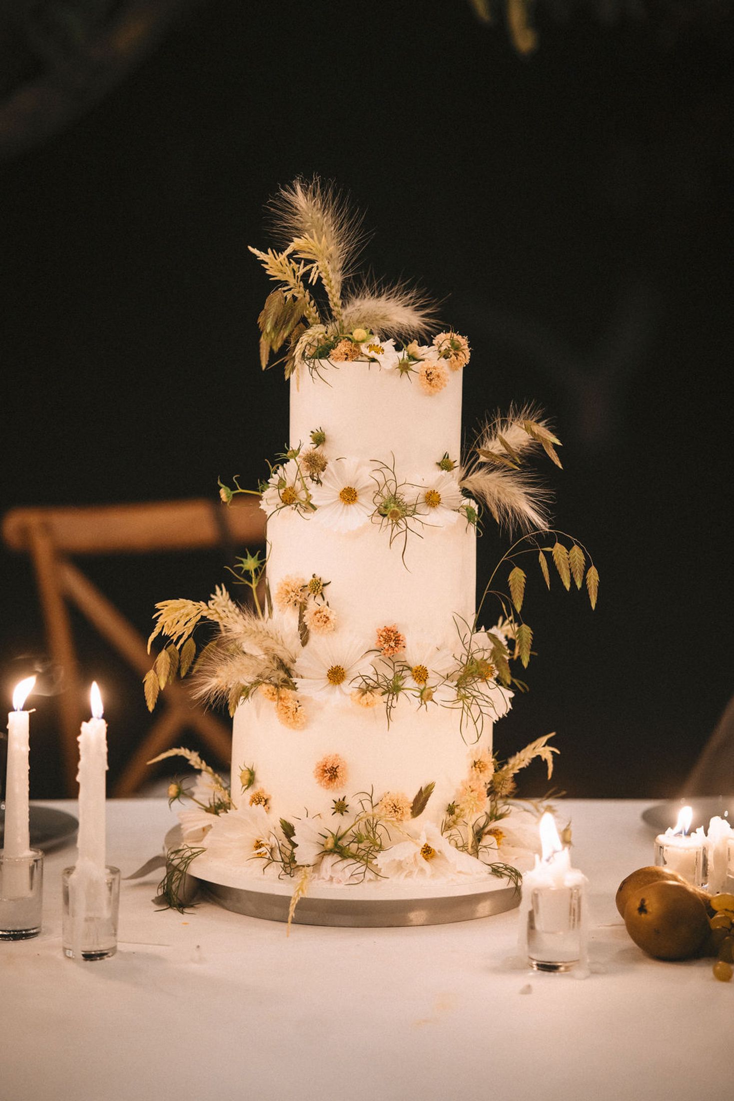 Elegant white wedding cake decorated with gold stars and feathers illuminated by candlelight in a dark setting.