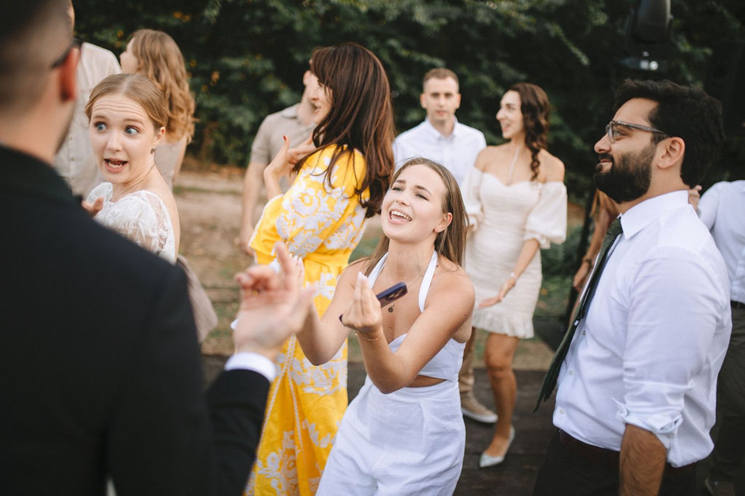 A joyful outdoor celebration with people dancing and laughing together in casual summer attire.