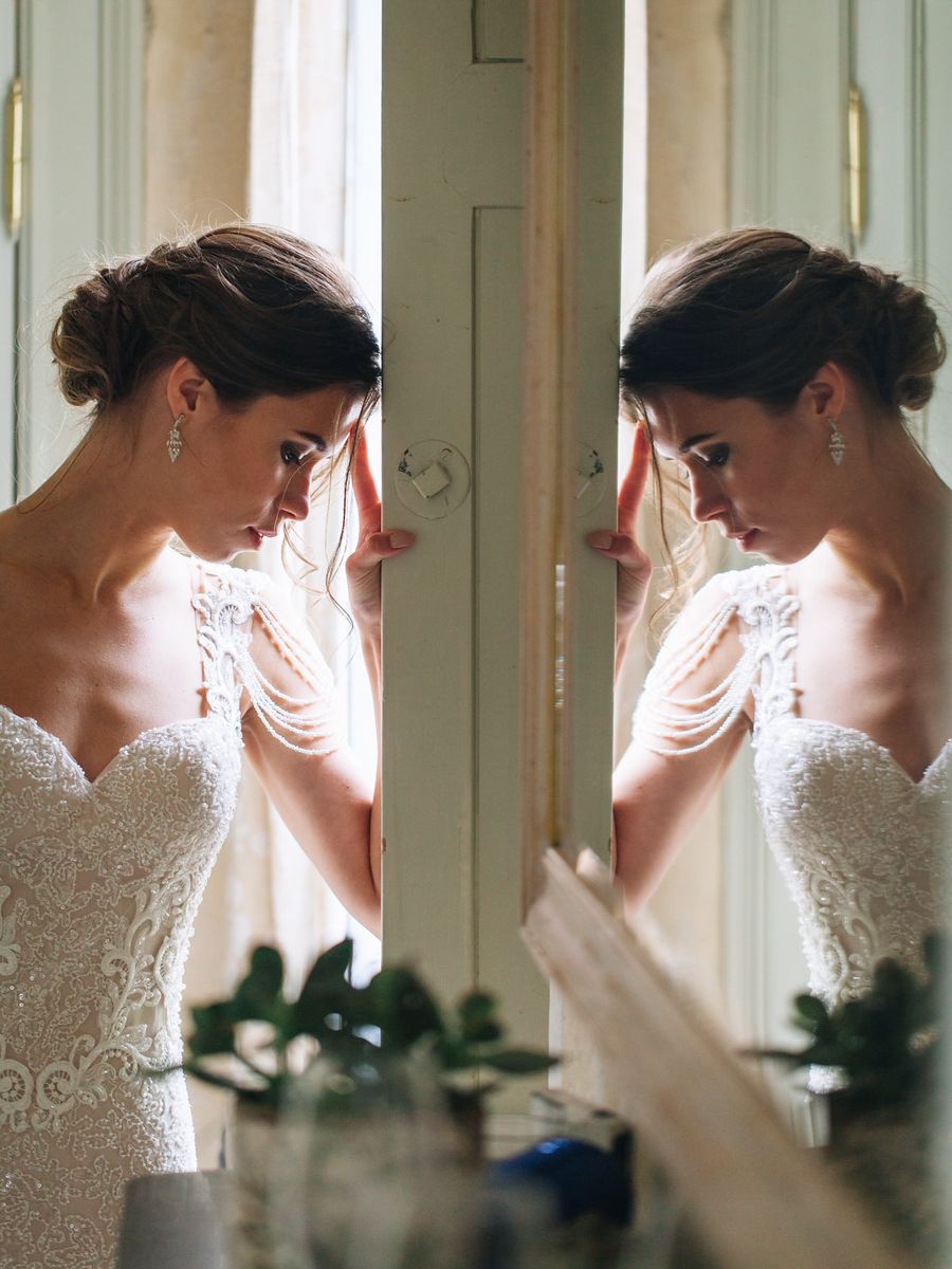 Multiple window reflections show a bride in a delicate lace gown looking down in elegant side profile.