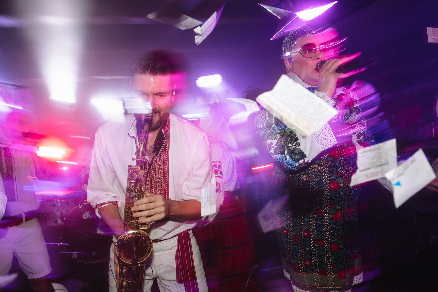 Motion blur capture of dancers moving under vibrant purple and pink stage lighting.