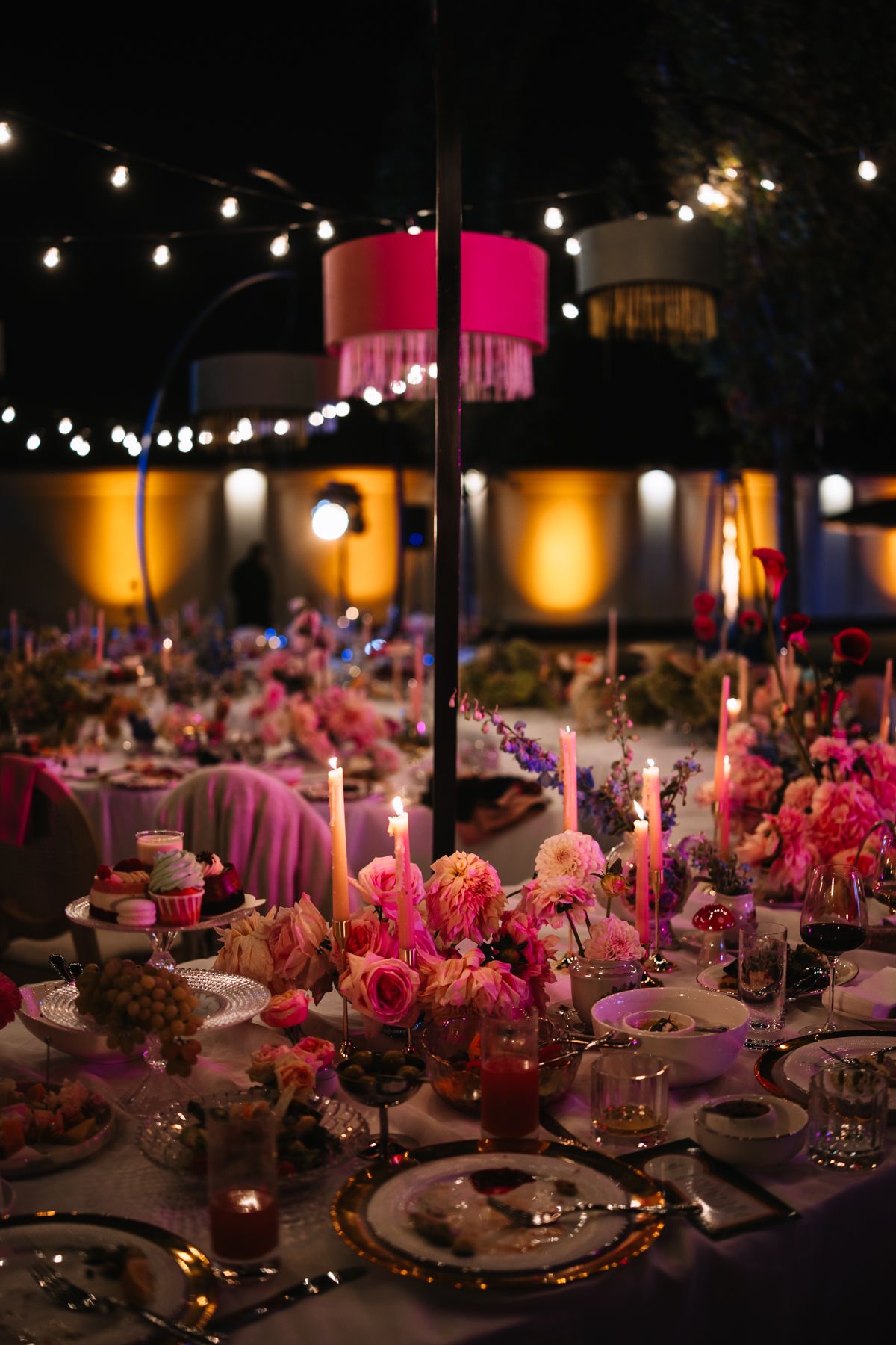 Elegant wedding reception table setting with pink floral centerpieces and string lights creating a romantic ambiance.
