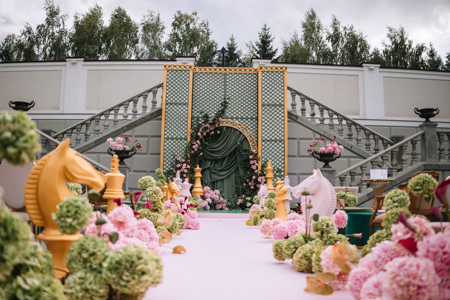 Colorful dinosaur figurines arranged among pink flowers and greenery in an outdoor garden setting.