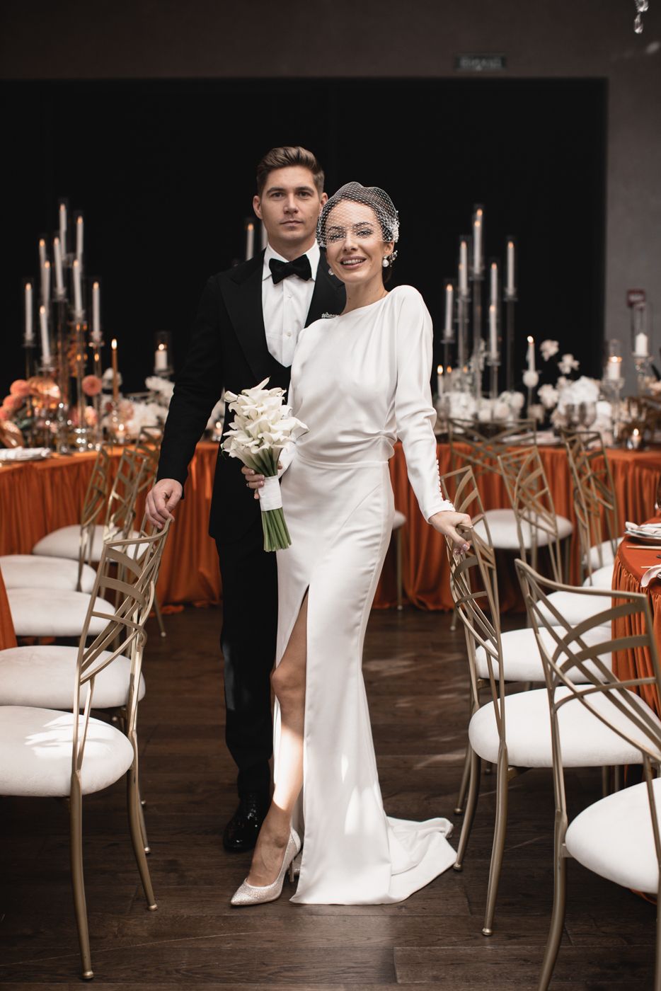 Elegant wedding reception setup with white chairs and orange accents.