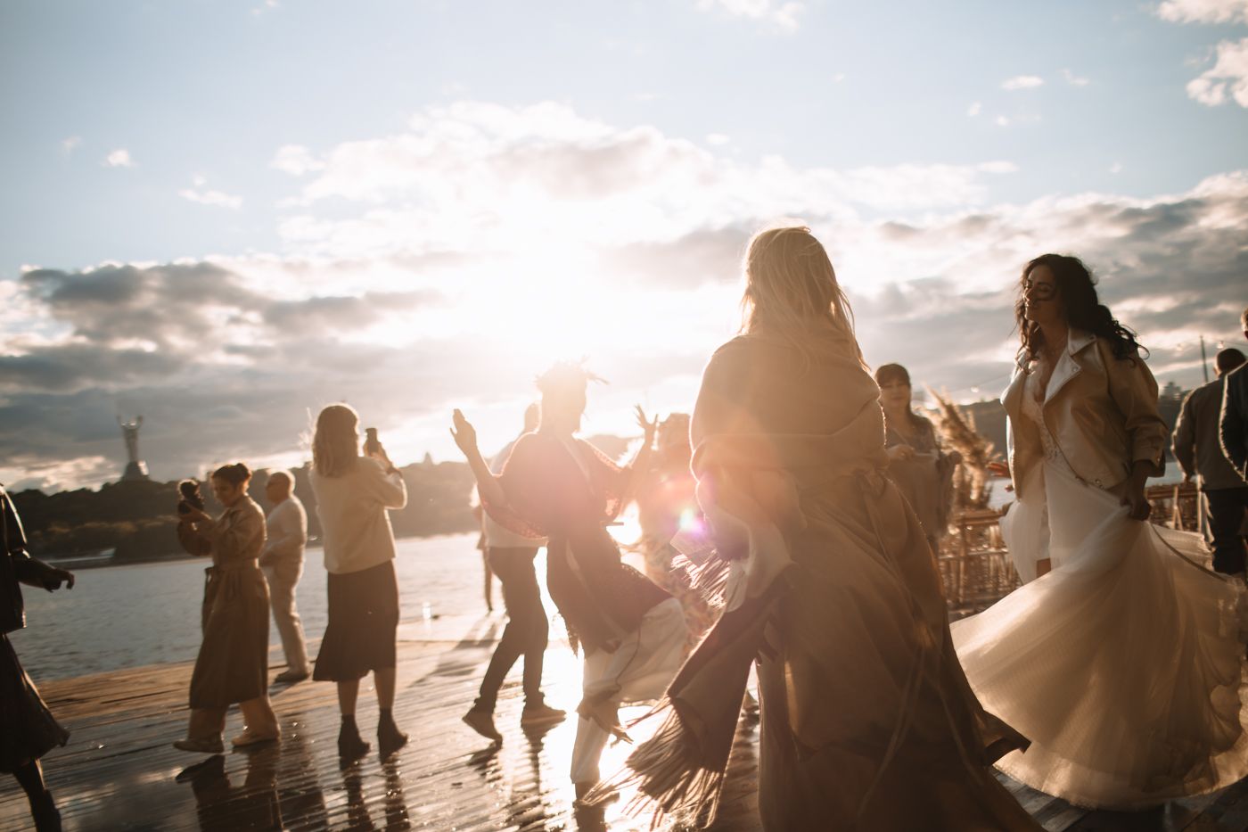 Silhouettes of people dancing at an outdoor celebration during sunset with dramatic backlit sky.