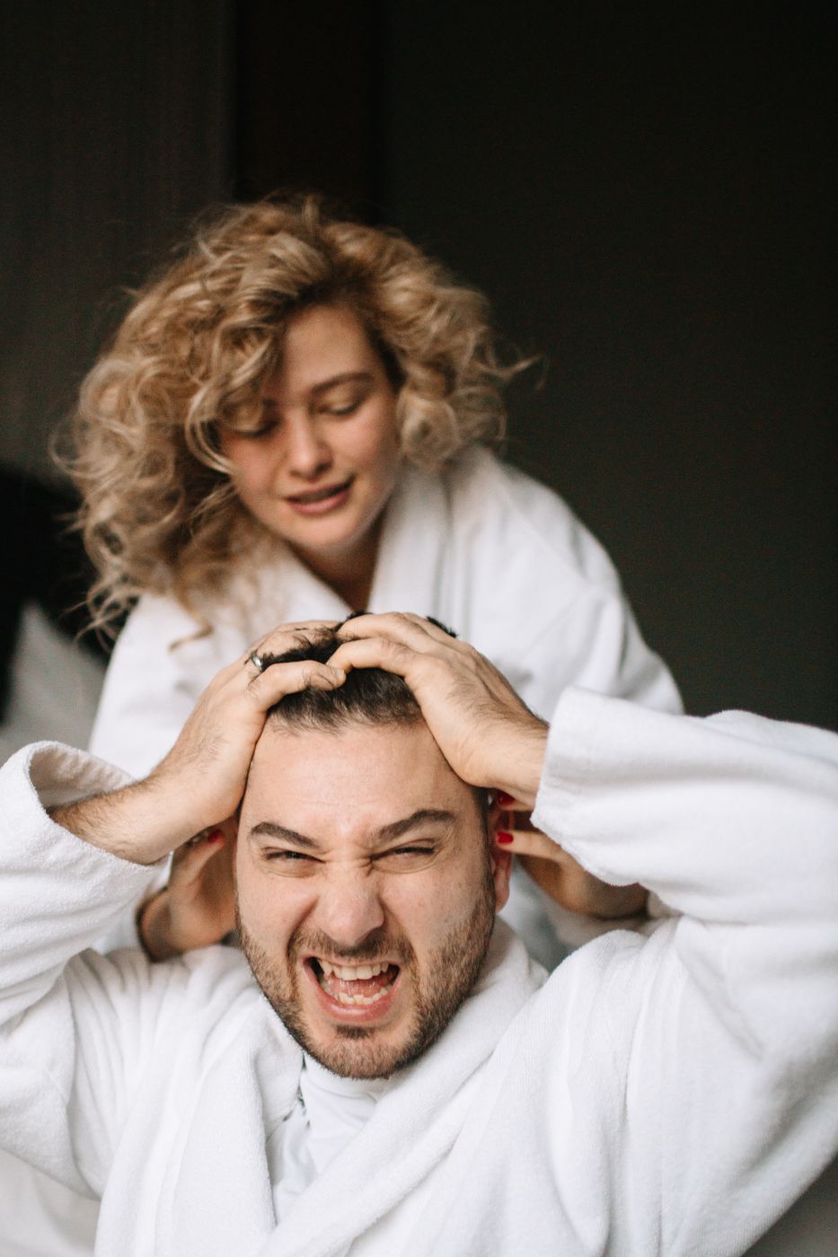 A playful couple in white bathrobes share a joyful moment together with tousled blonde hair and laughter.