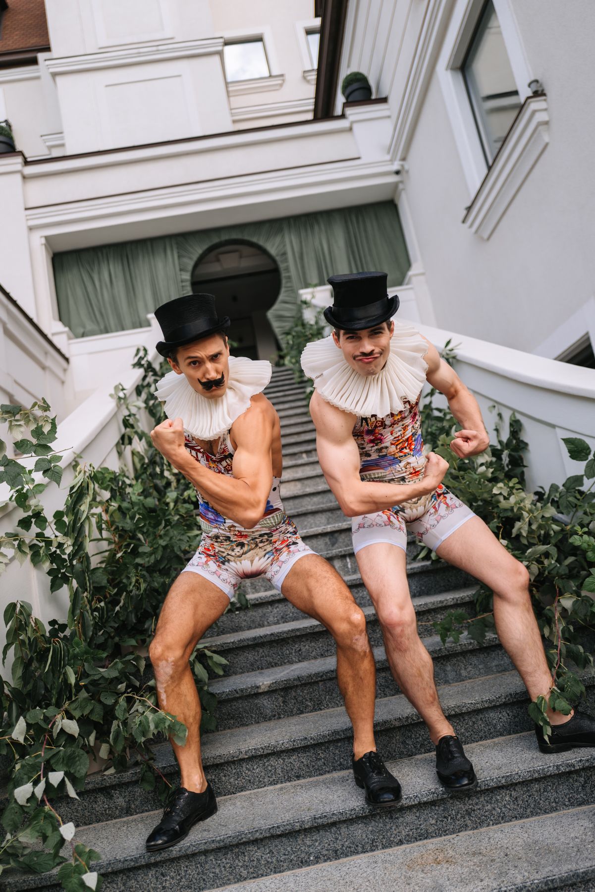 Two people in shorts and boots sit on outdoor stone steps while laughing together in a playful series of poses.