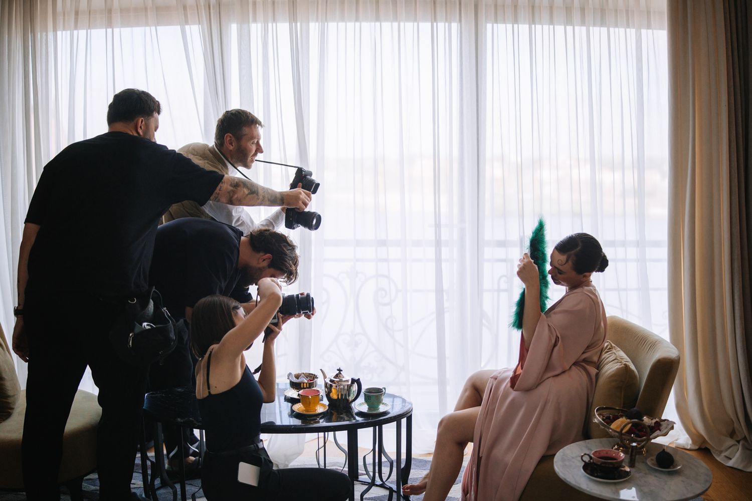 Professional photographers work at a photoshoot in a bright room with white curtains and natural lighting.