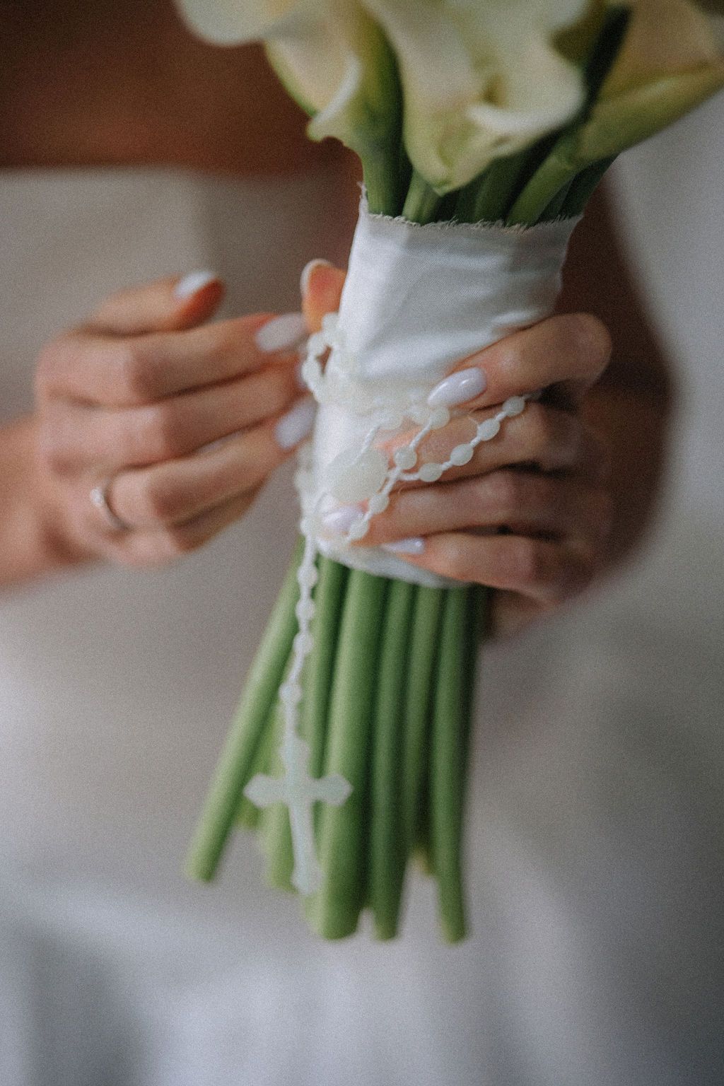 Hands holding an elegant white calla lily bouquet wrapped in lace-trimmed fabric for a wedding ceremony.