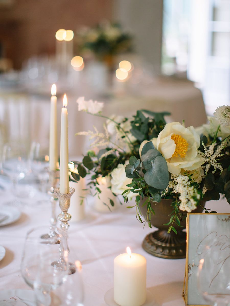 Elegant wedding table setting with white flowers, eucalyptus, candles and crystal glassware on a white tablecloth.