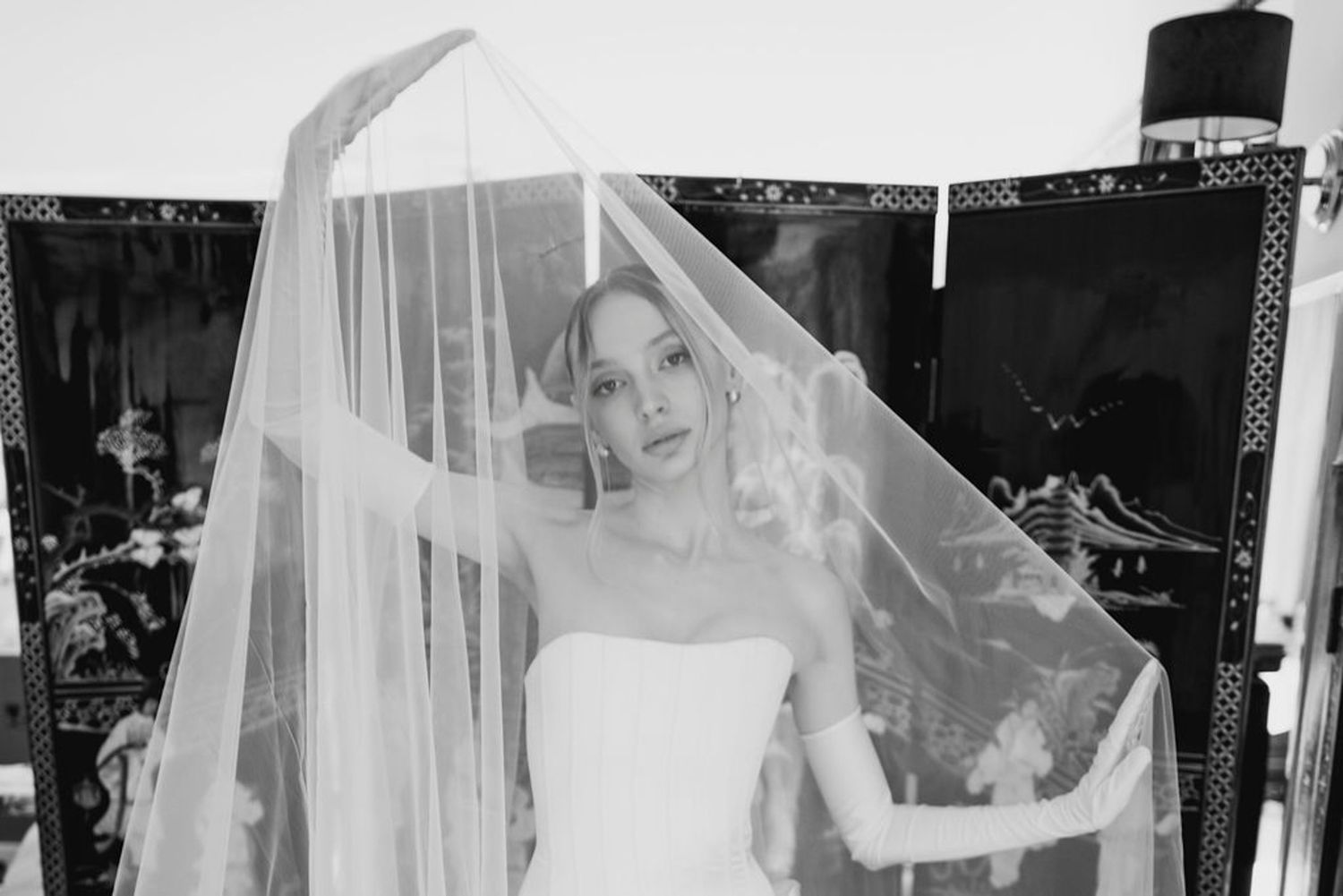 A bride in a white wedding dress and veil walks through a black and white archway in an artistic composition.