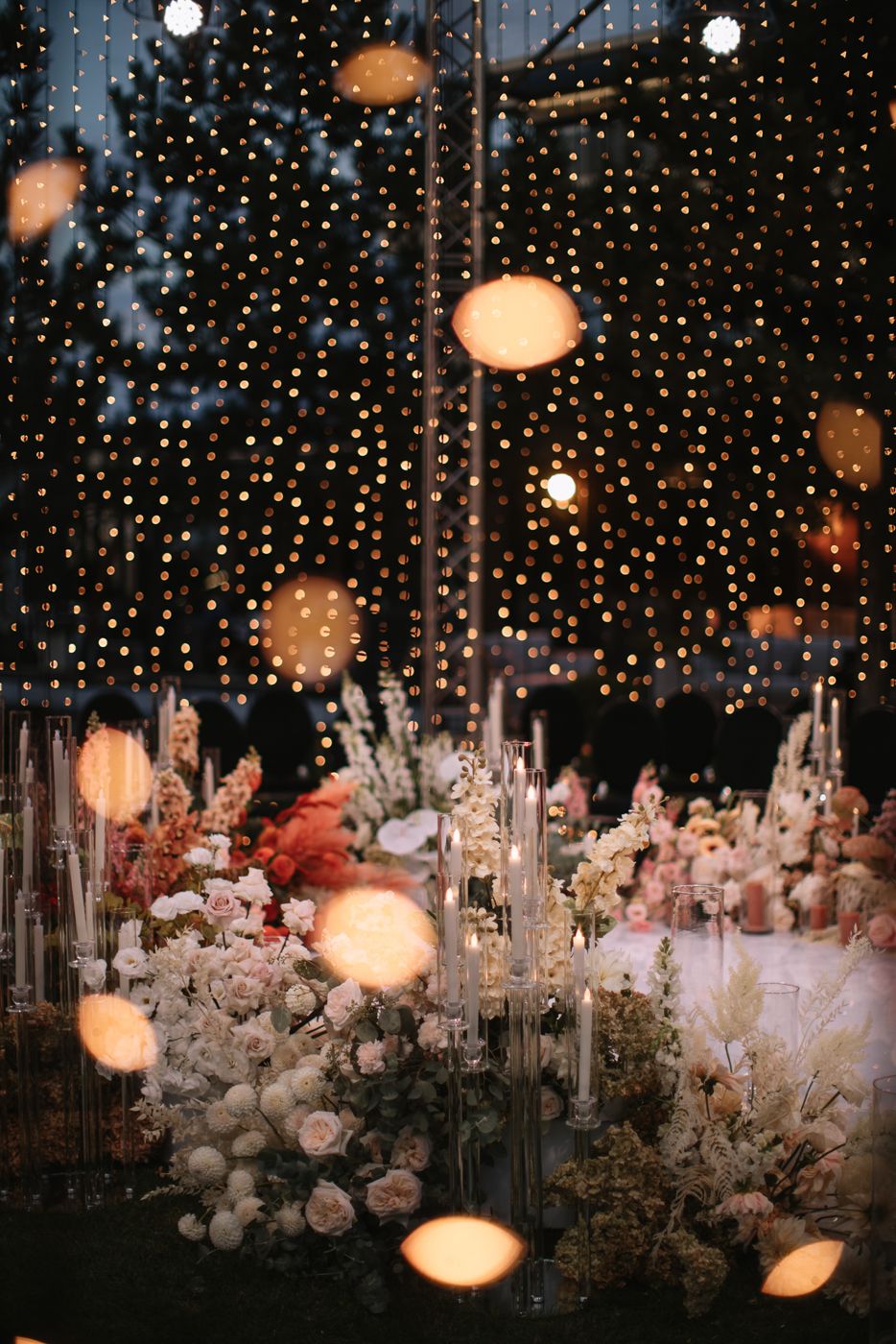 Romantic wedding decor with hanging lights, candles and white floral arrangements creating a magical atmosphere.