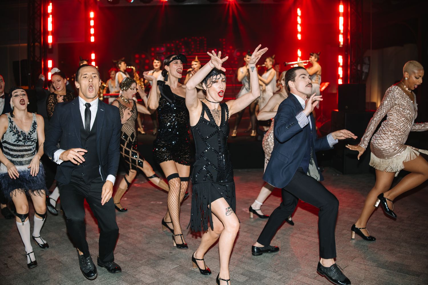 People dancing at a lively nighttime event with red lighting and formal attire.