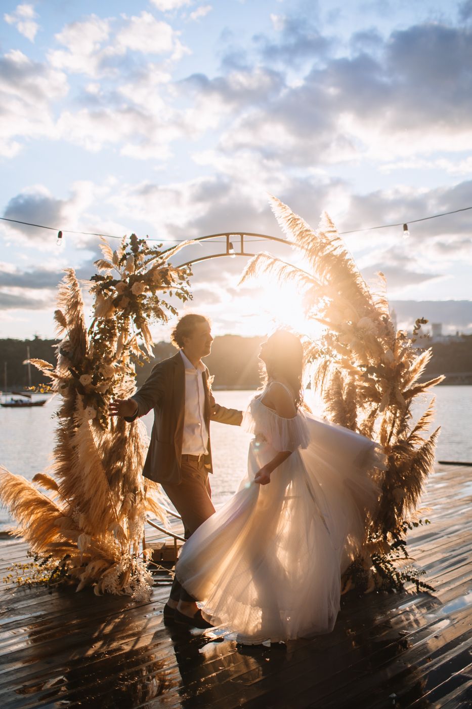 A romantic sunset beach wedding scene with pampas grass decor and string lights creating a dreamy atmosphere.
