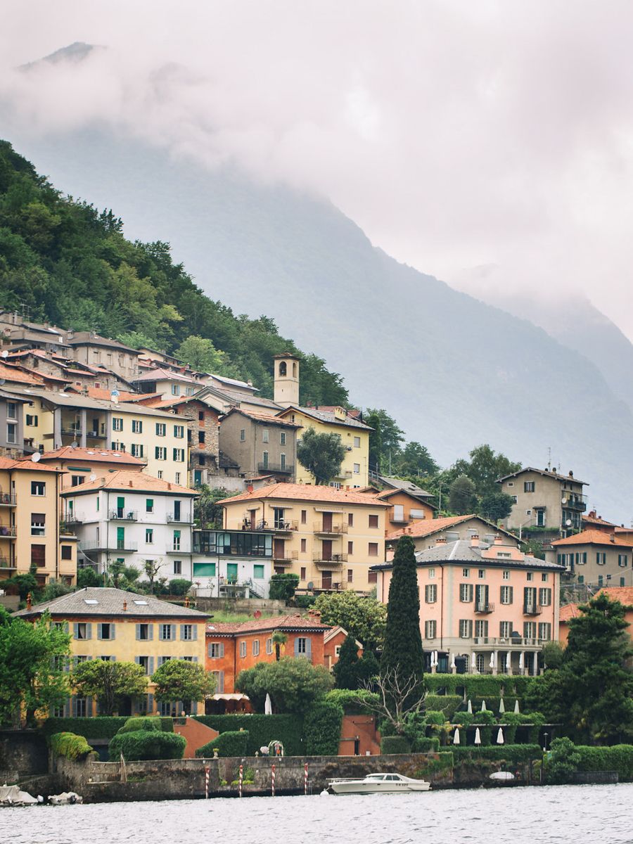 Charming hillside village with colorful Italian houses and a church tower overlooking Lake Como on a misty day.