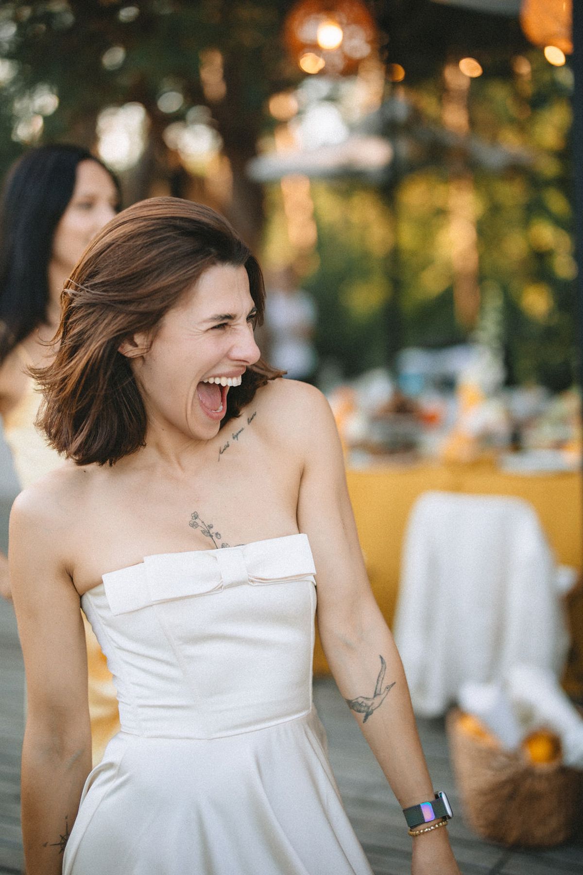 Woman in white strapless dress laughs joyfully during outdoor photo session with warm evening lighting.