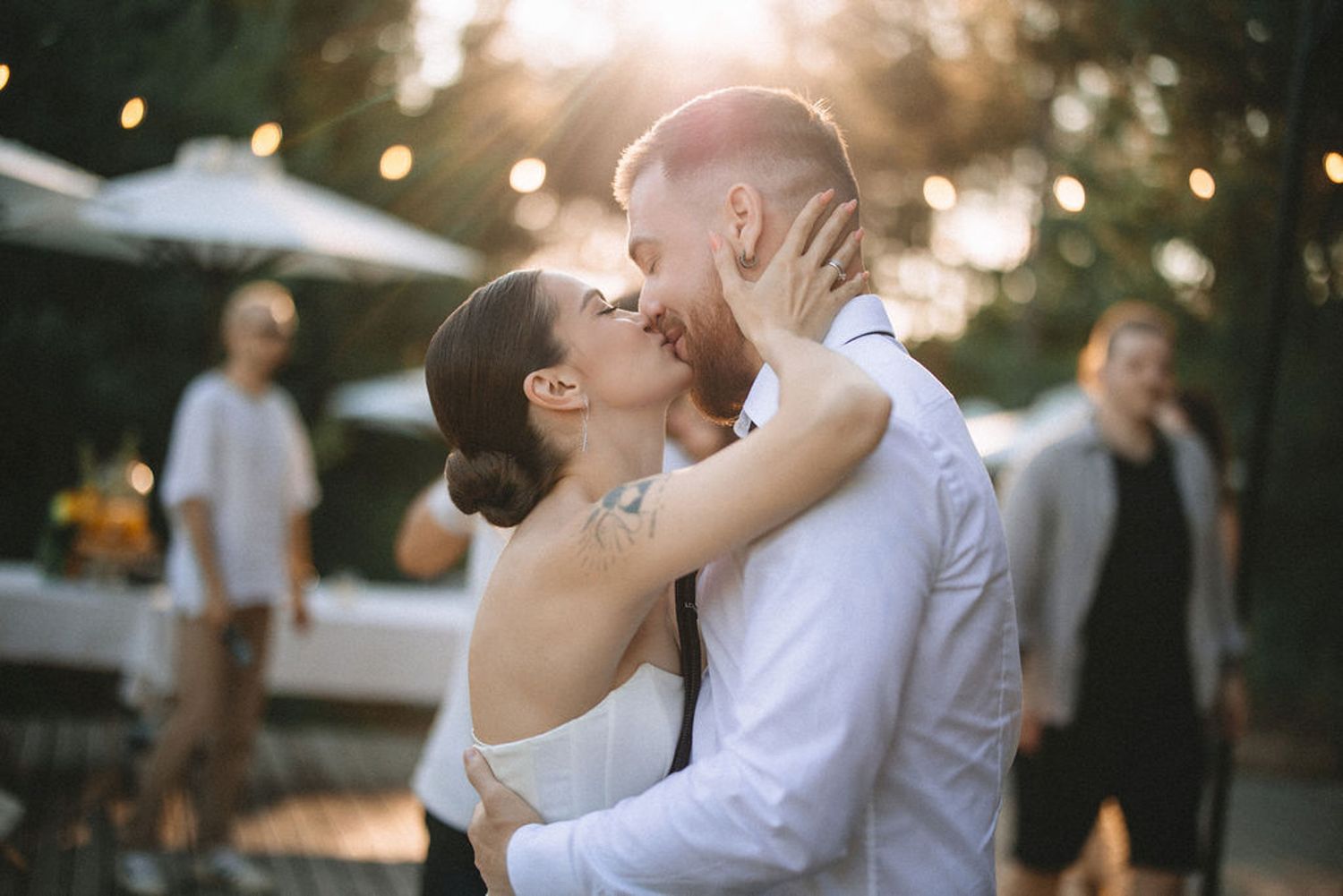 A romantic wedding couple shares a tender embrace and kiss during their outdoor reception celebration.