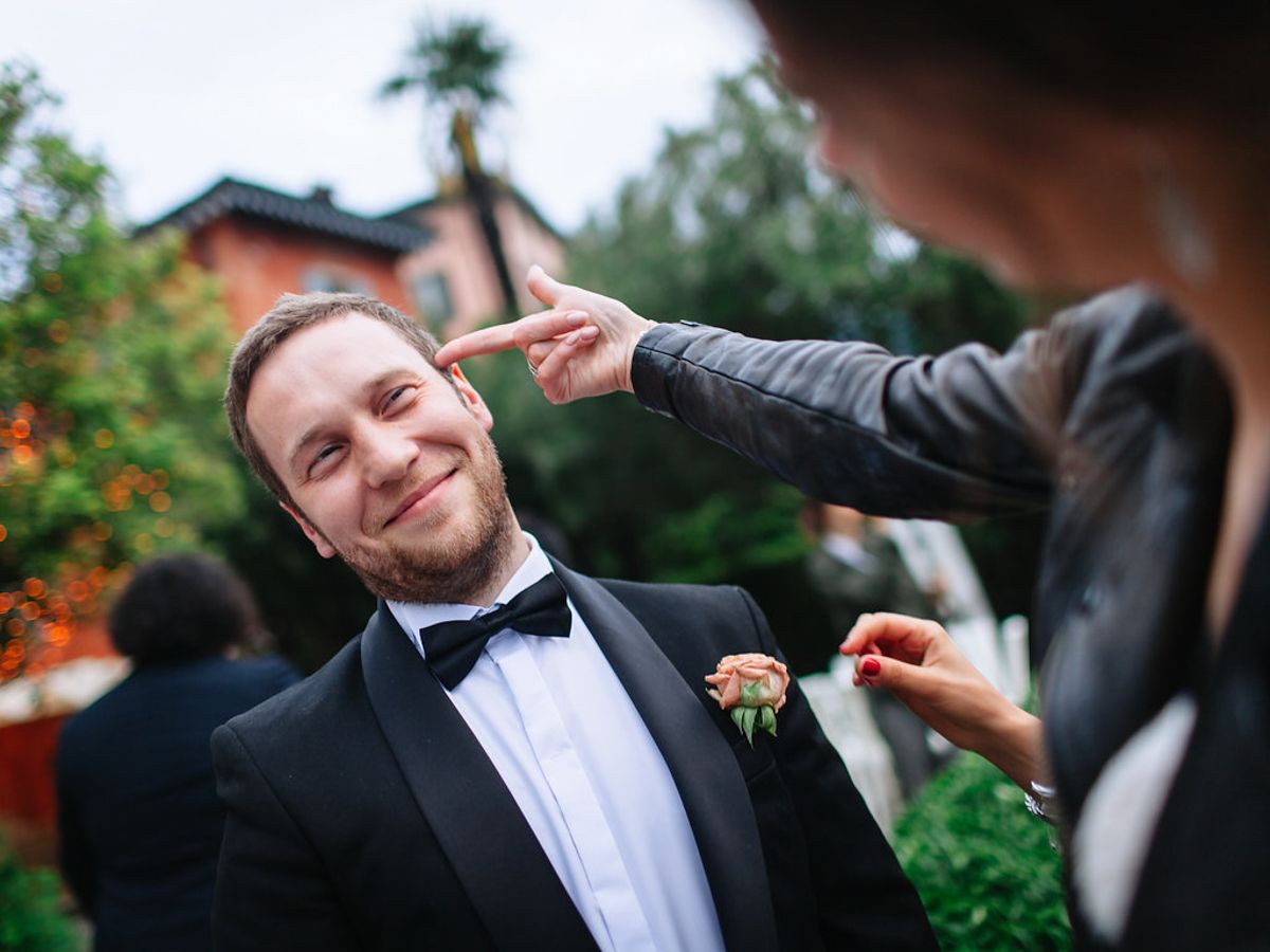 A group of people in formal attire share laughs and smiles at an outdoor wedding celebration.