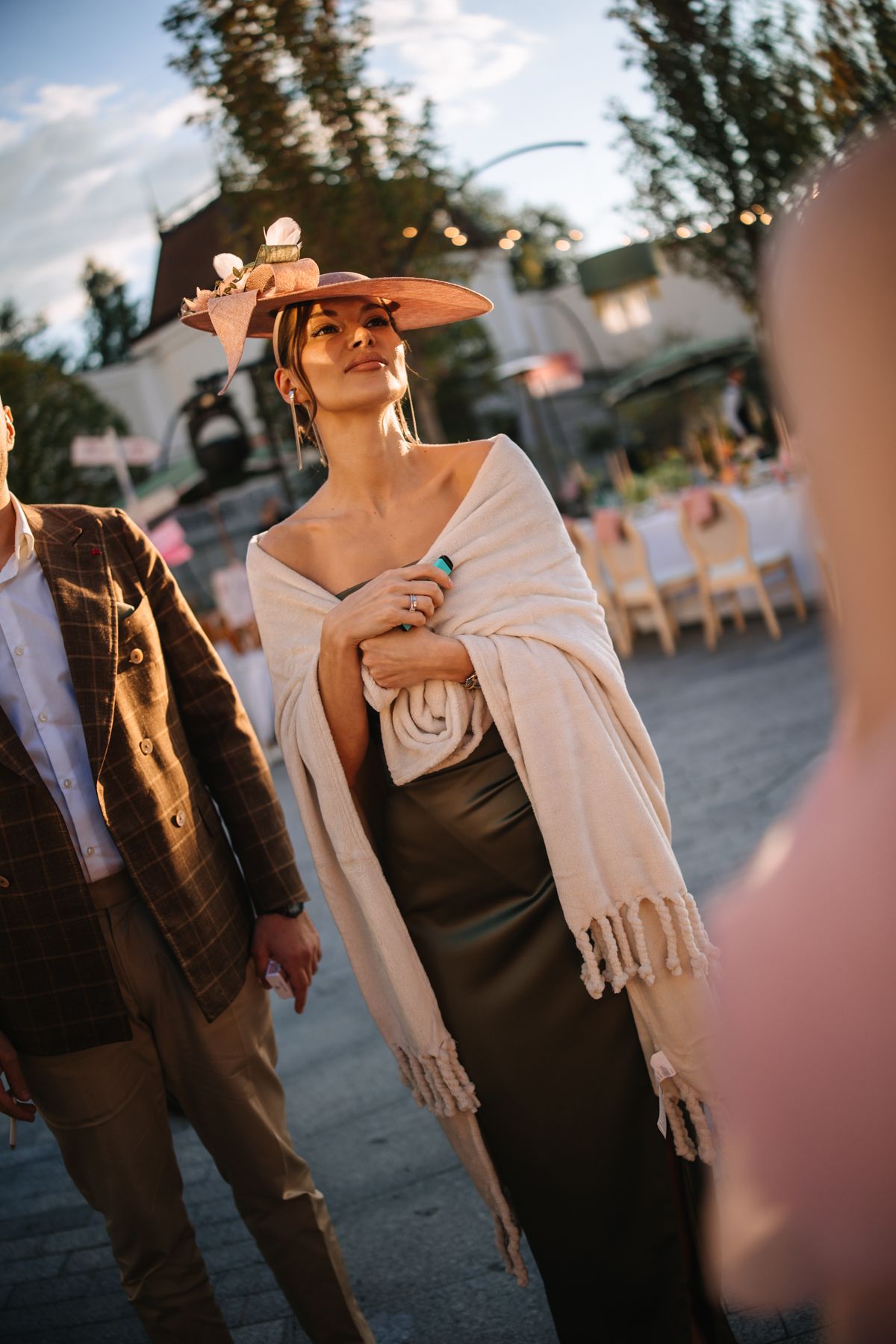Guests in formal attire mingle at an outdoor evening event with a warm sunset glow.