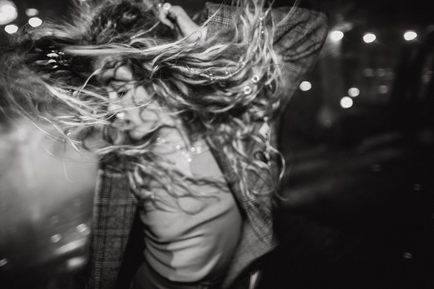 Black and white photograph of hair blowing in the wind with bokeh lights creating a dreamy nighttime atmosphere.