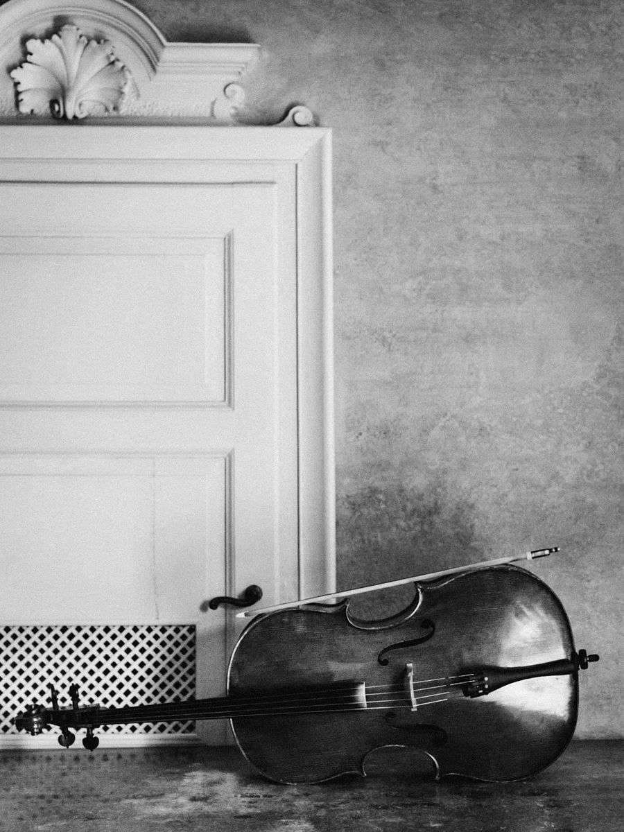 A black and white photograph of a cello resting against a white door with ornate molding and decorative details.