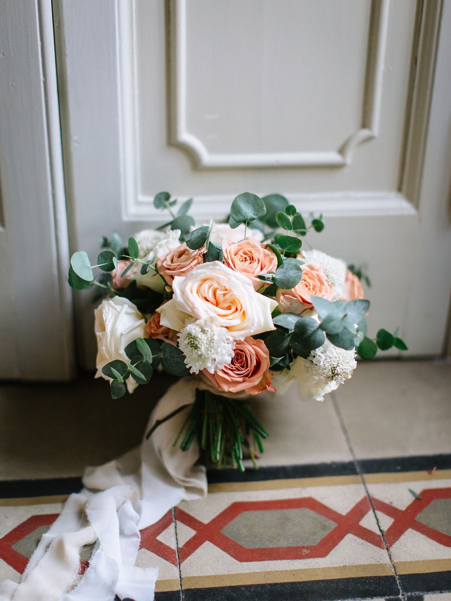 A romantic bouquet of peach roses and white flowers with green foliage arranged on a white windowsill.
