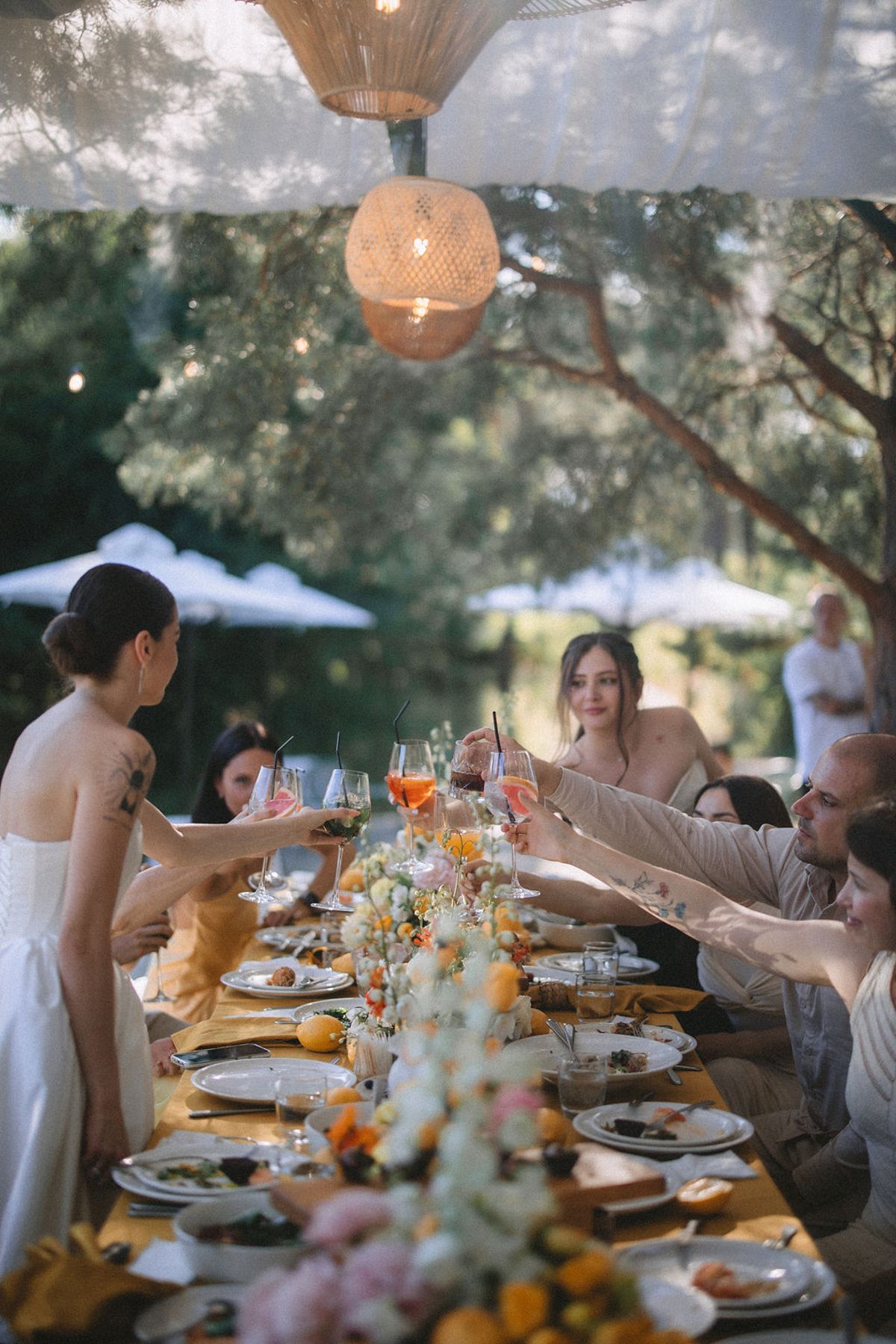 People enjoying an elegant outdoor dinner party under string lights with orange and white floral table decorations.