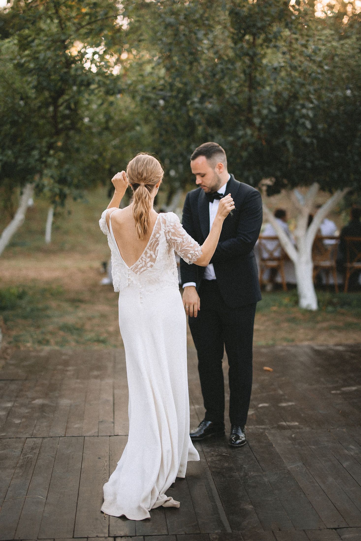 A couple dances romantically on a wooden deck surrounded by trees at sunset during their wedding celebration.