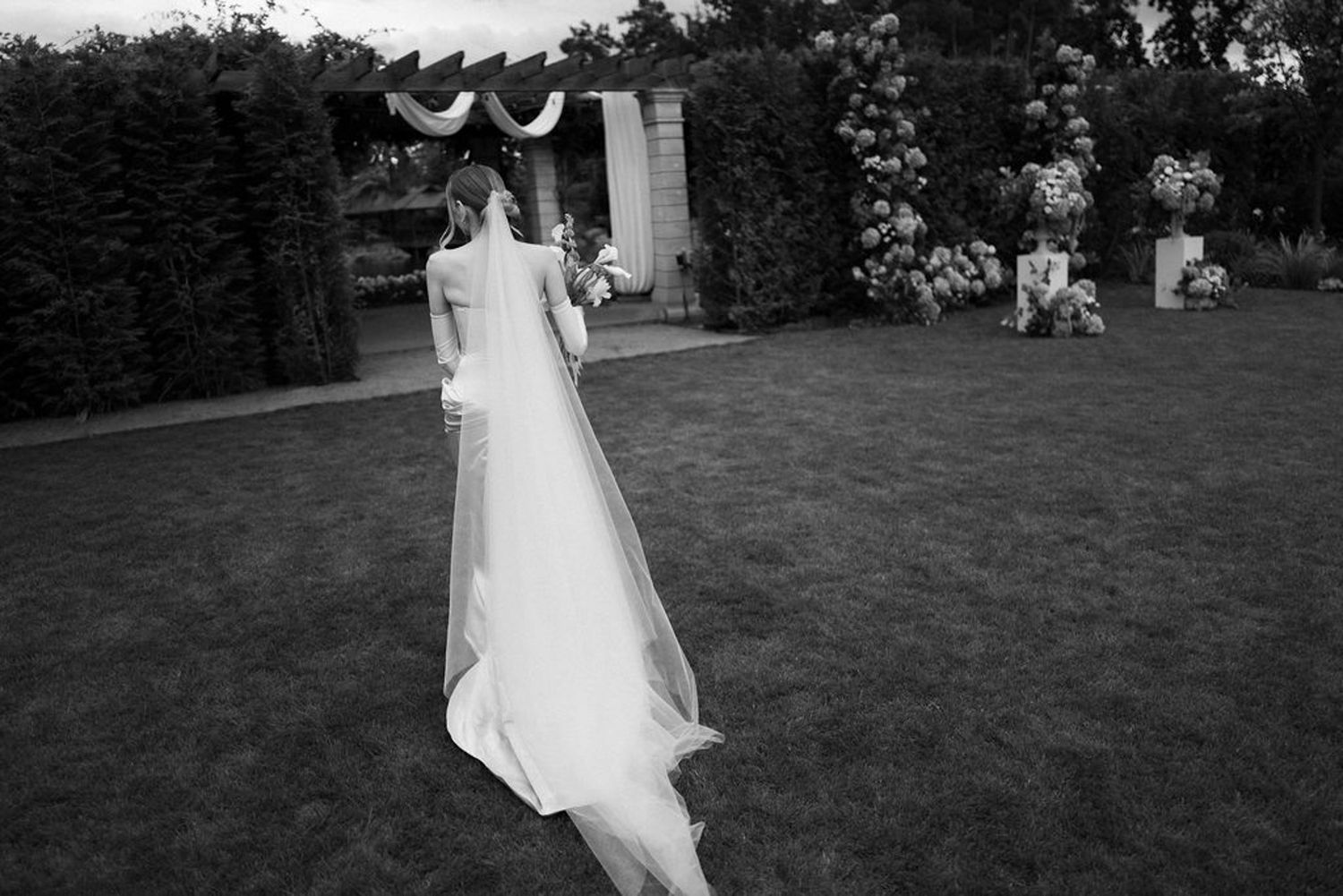 A person in a white wedding dress walks across a lush green lawn during an outdoor celebration.