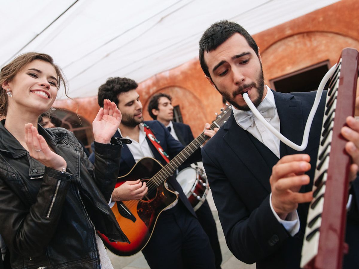Musicians in suits perform together in a dynamic group shot showing violins and other instruments being played.