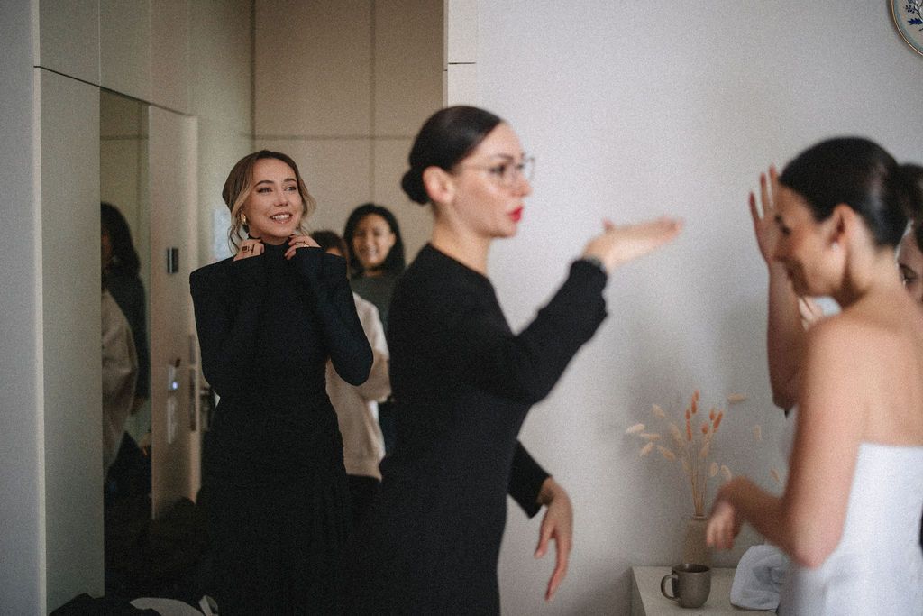 People in formal attire gather in a room, with one wearing a black dress and another in a white gown.