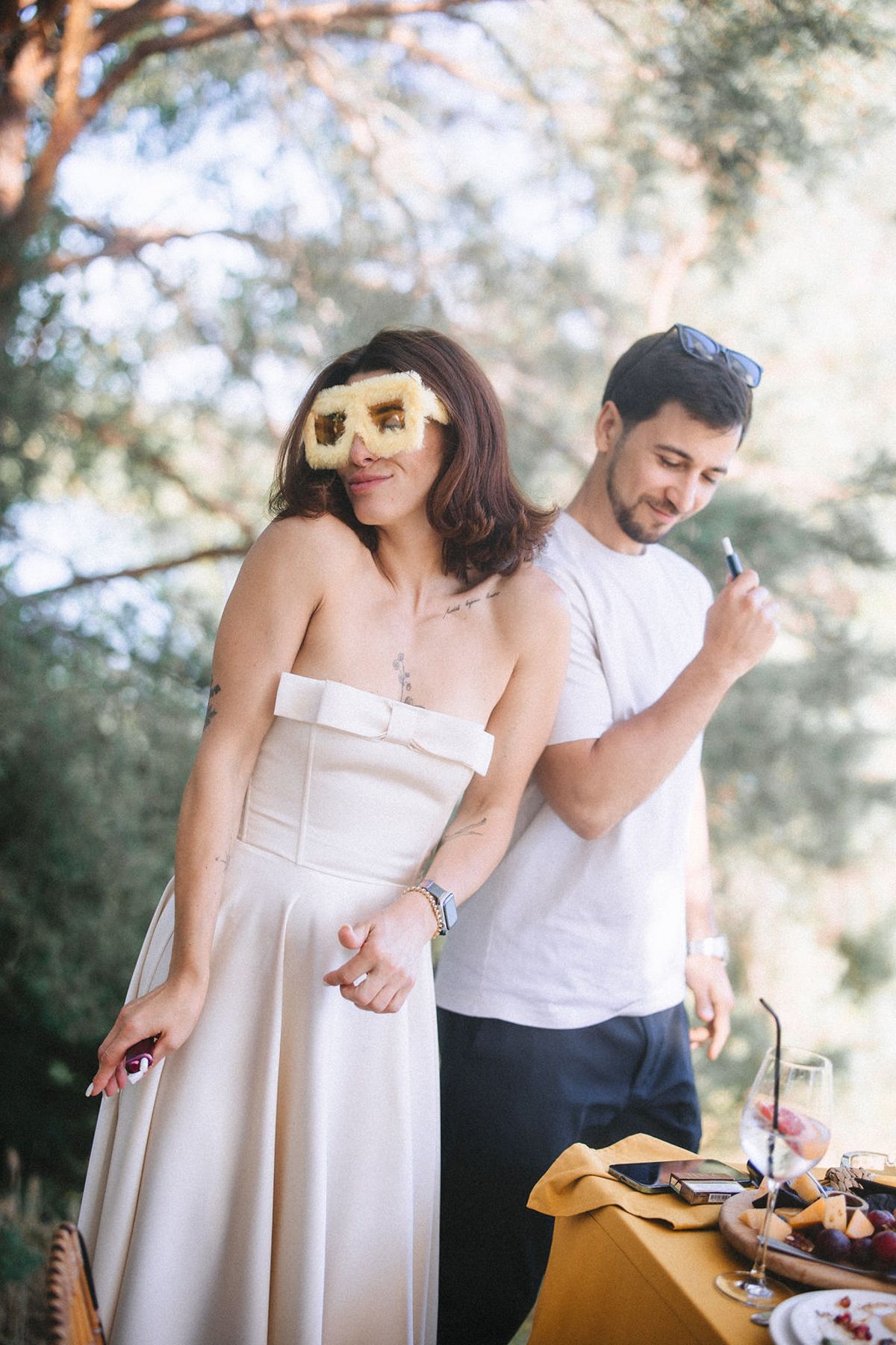 A couple in light colored outfits enjoys an outdoor picnic together on a sunny afternoon.