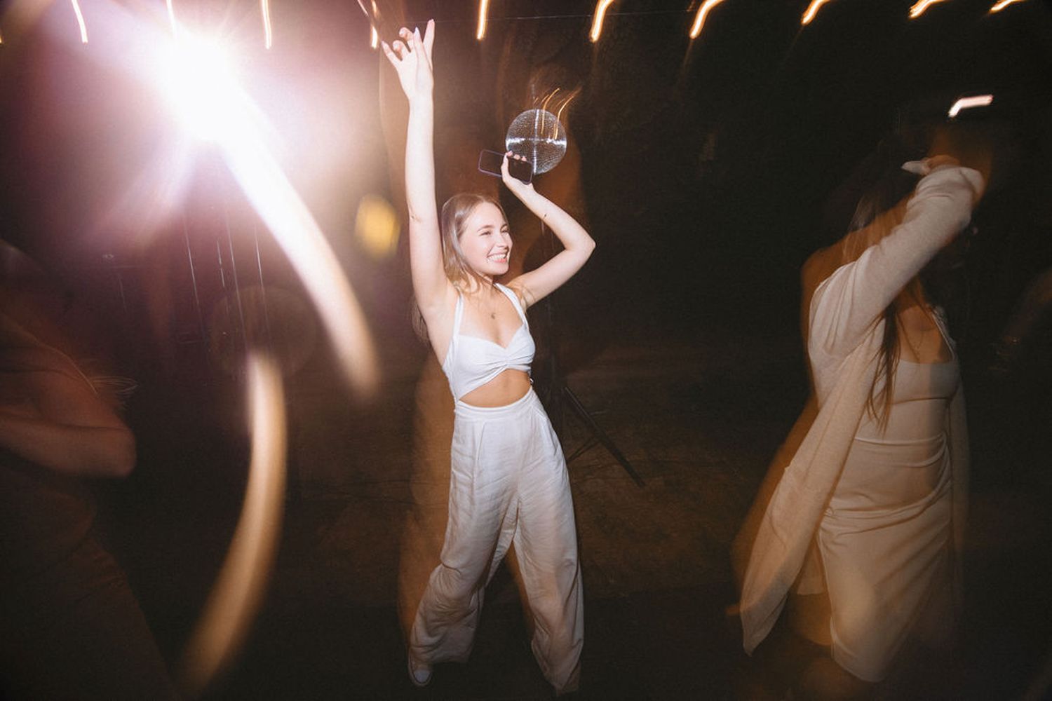 Partygoers dancing at night with sparklers and light trails creating a dreamy atmosphere at an outdoor celebration.