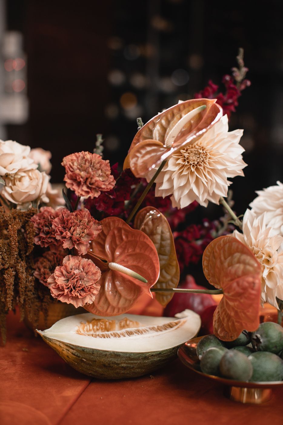 Close-up of peach and coral floral arrangements with dahlias and anthurium on a rustic table setting.