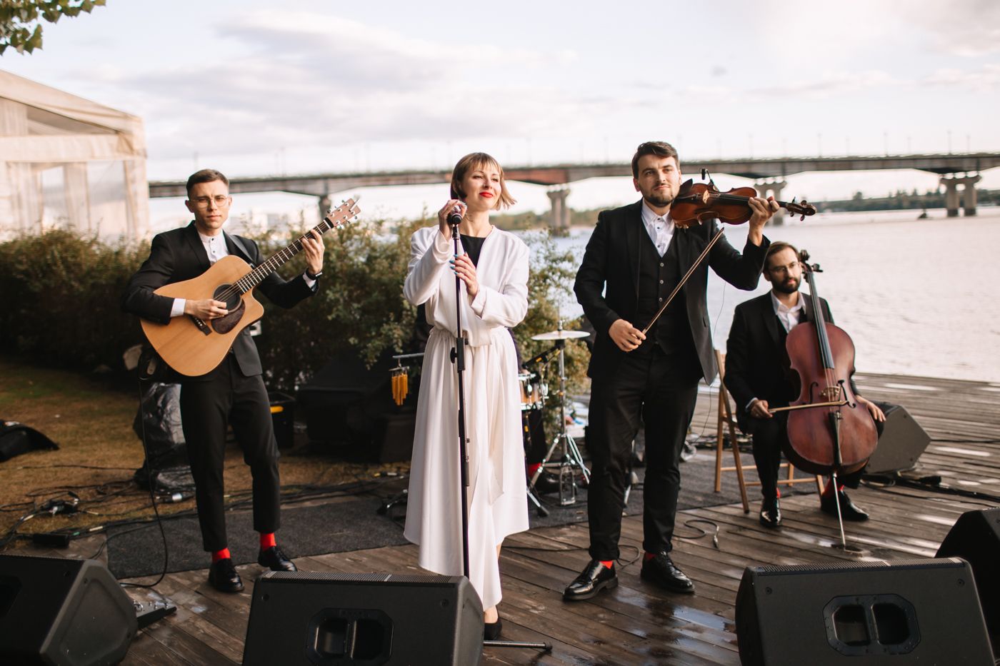 A string quartet performs music outdoors by the waterfront at sunset during an elegant event.