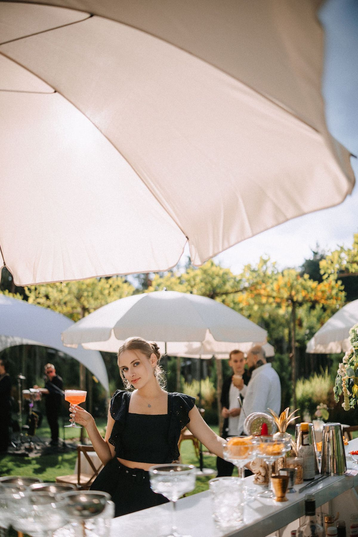 Outdoor event setup with white umbrellas and tables arranged for dining in a garden setting during daytime.