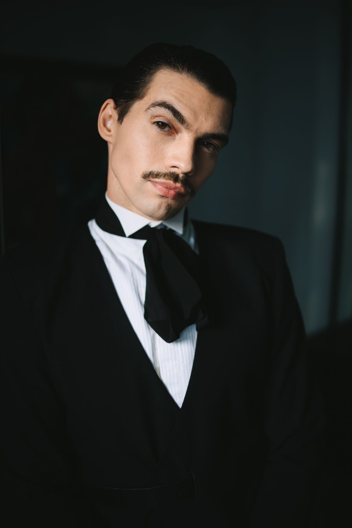 Dramatic black and white portrait series showing someone in a tuxedo and bowtie against dark shadows.