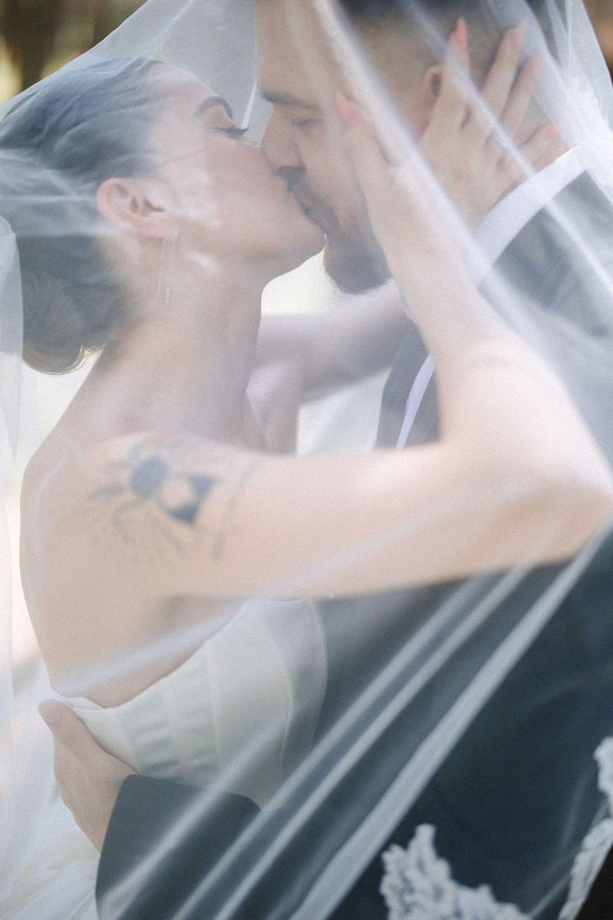 A romantic wedding moment captured through a delicate veil as newlyweds share an intimate kiss.