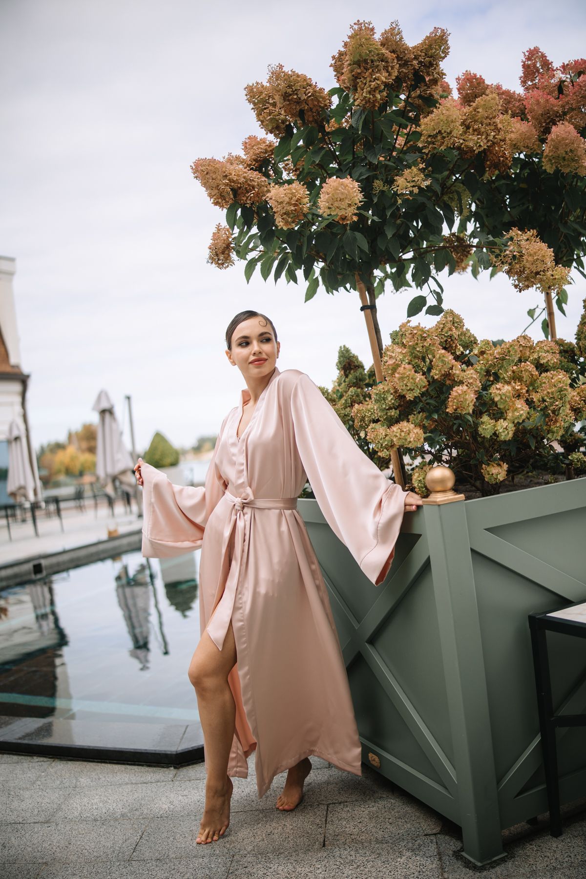 Soft pink dress flowing in the breeze against large beige hydrangea blooms in outdoor planters.